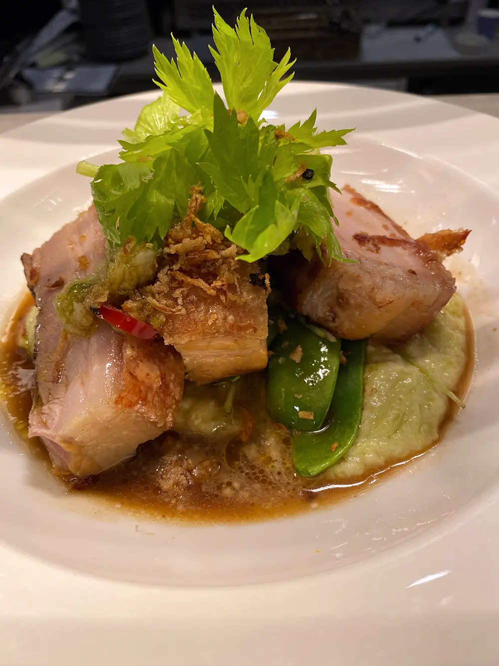 Close-up of a gourmet pork dish with vegetables and sauce, prepared using high-quality extra virgin olive oil suitable for high-heat cooking, highlighting flavor and nutrition.