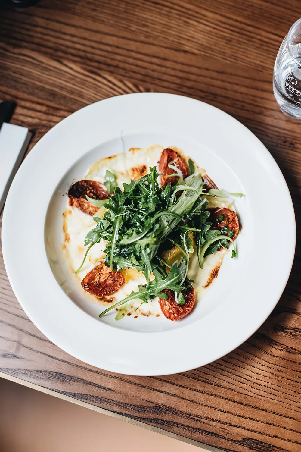 Fresh arugula salad with roasted tomatoes drizzled with extra virgin olive oil, demonstrating a healthy way to combine olive oil with antioxidant-rich foods for enhanced nutrition.