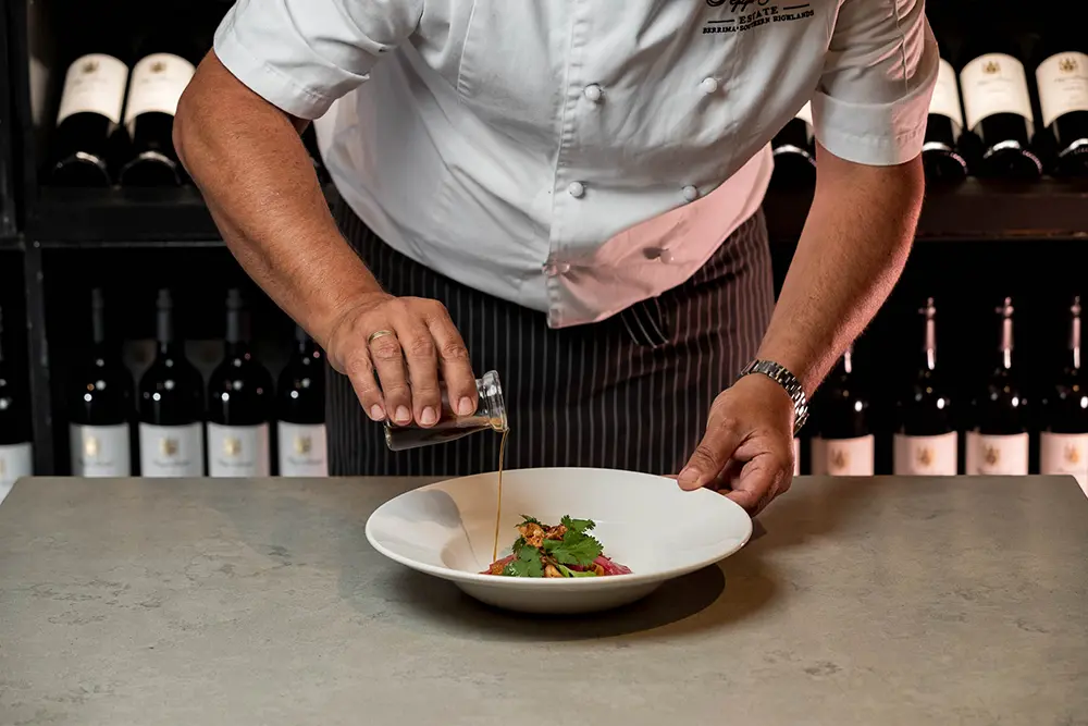 Chef drizzling extra virgin olive oil on a gourmet pasta dish in a fine dining restaurant setting.