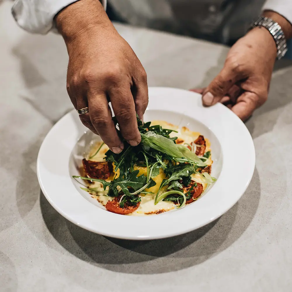 Chef garnishing a fresh salad with arugula and roasted vegetables, highlighting the use of olive oil in everyday cooking to enhance flavor and support digestive health.