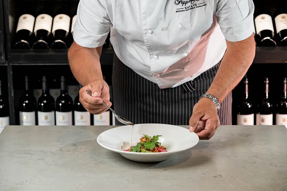 Chef plating garlic olive oil pasta with fresh herbs in a fine dining kitchen setting.