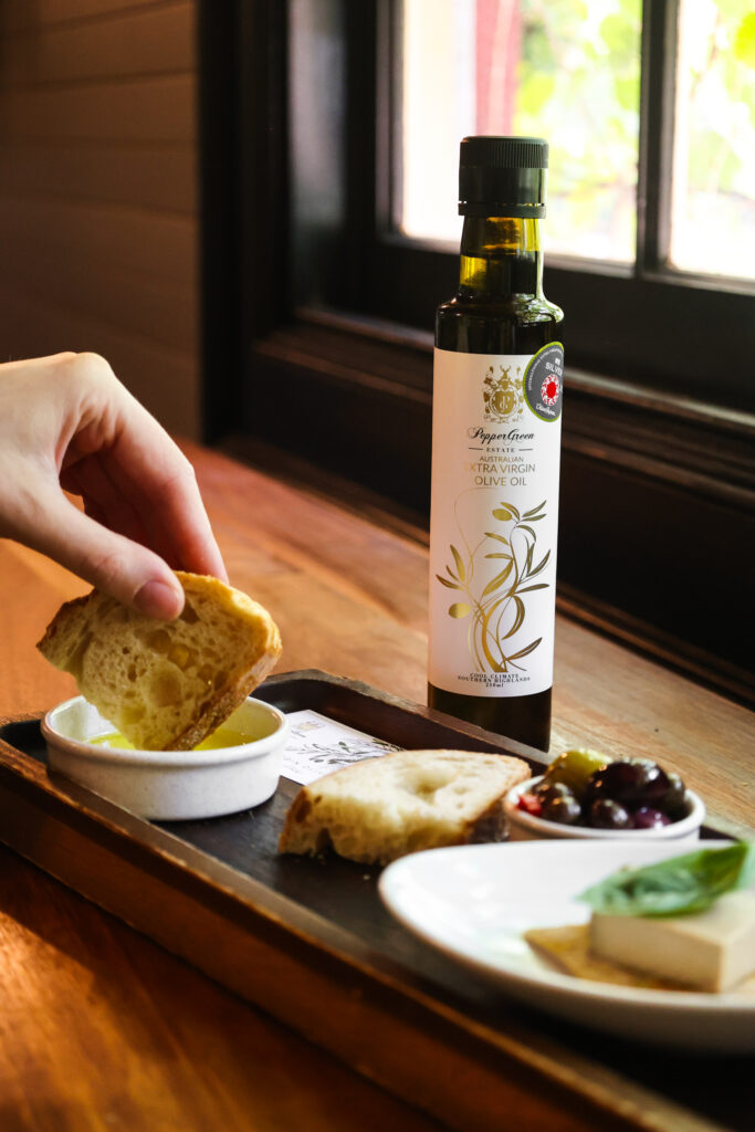 Hand dipping fresh bread into PepperGreen Estate extra virgin olive oil, demonstrating the safety and deliciousness of eating cold-pressed olive oil raw in Mediterranean and cold appetizer recipes