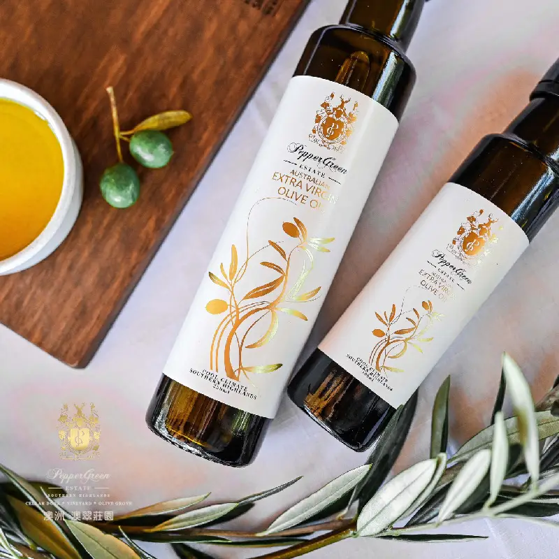 幾瓶橄欖油擺放在木板上，旁邊放著青橄欖和橄欖枝。