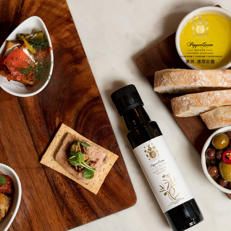 PepperGreen Estate olive oil, a top choice for deep frying, displayed with an appetizer spread, olives, and baguette.